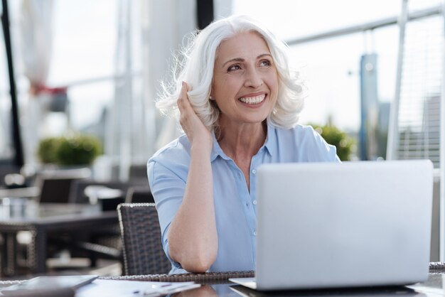 Felice donna che mantiene il sorriso sul suo viso e seduto davanti al suo computer mentre guarda verso l'alto