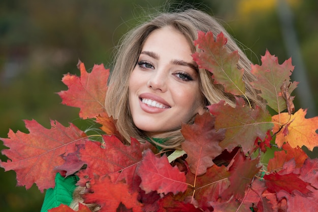 Felice donna con foglie d'autunno sul viso in autunno natura Ritratto di giovane donna con autunno acero le