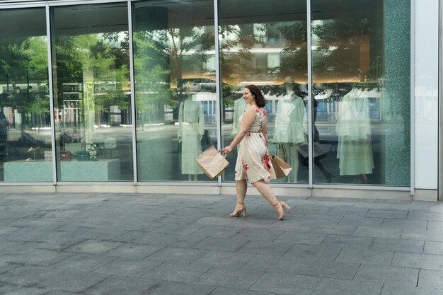 Felice donna curvy con borse della spesa artigianali ecologiche guardando la vetrina del negozio godendo nello shopping Concetto di stile di vita dello shopping consumistico
