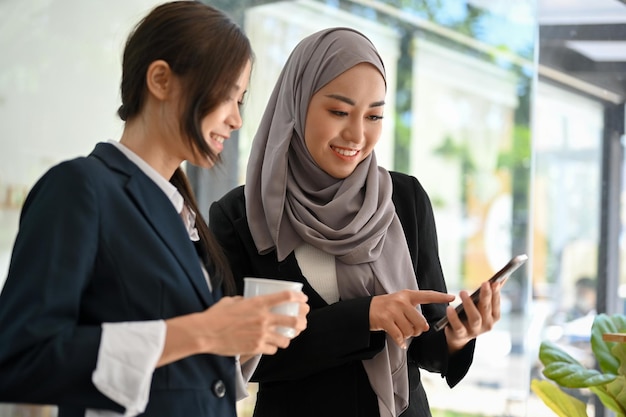 Felice donna d'affari musulmana asiatica che chiacchiera con la sua collega durante la pausa pranzo