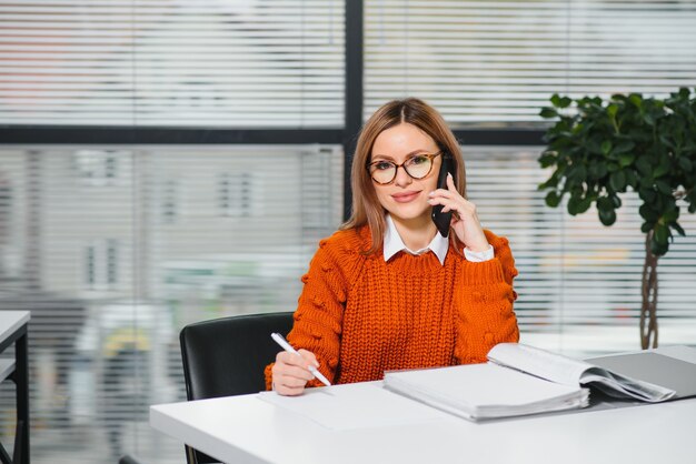 Felice donna d'affari sorridente al lavoro parlando al telefono, seduto al suo posto di lavoro in ufficio, copia dello spazio