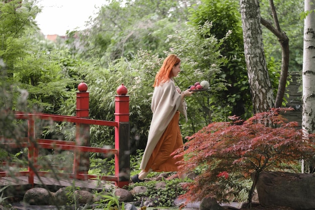 Felice donna dai capelli rossi che cammina in un parco o in un giardino ben curato con frutta libertà e modo sano
