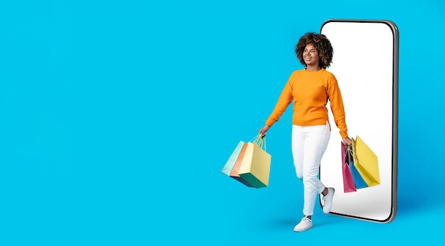 Felice donna di colore shopaholic che esce dal grande mockup del telefono