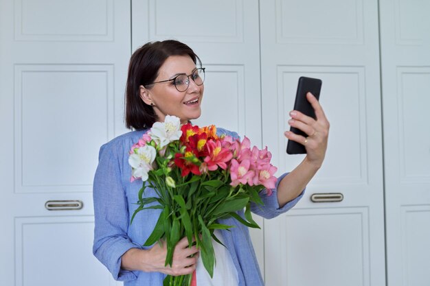 Felice donna di mezza età con un grande mazzo di fiori e smartphone