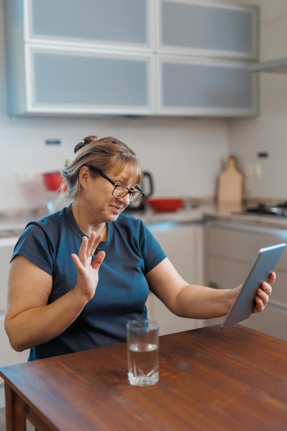 Felice donna di mezza età di 50 anni che utilizza tablet digitale seduto in cucina a casa