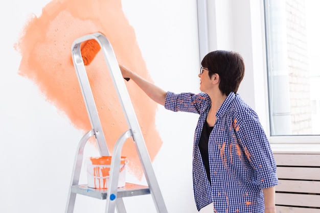 Felice donna di mezza età pittura muro nel suo nuovo appartamento. Ristrutturazione, ridecorazione e riparazione