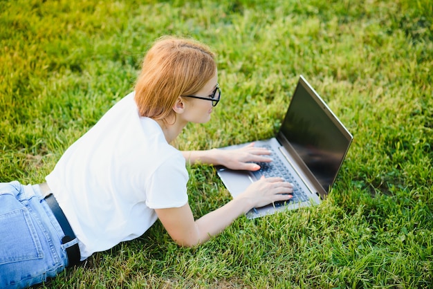 Felice donna di mezza età sdraiato sull'erba verde utilizzando il computer portatile nel parco