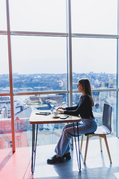 Felice donna europea che lavora online in caffetteria utilizzando laptop e spazio per la copia del caffè Libero professionista femminile di successo che digita sul laptop lavoro a distanza