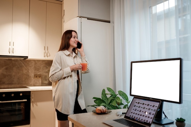 Felice donna freelance in abiti casual che parla al telefono con gli amici in piedi sulla cucina di casa durante il lavoro freno Ciao, piacere di conoscerti