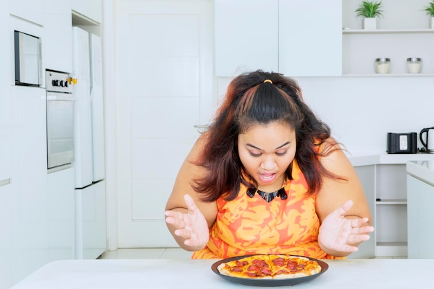 Felice donna grassa guardando un piatto di gustosa pizza