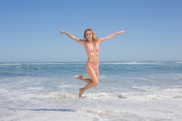 Felice donna in forma in bikini che salta sulla spiaggia