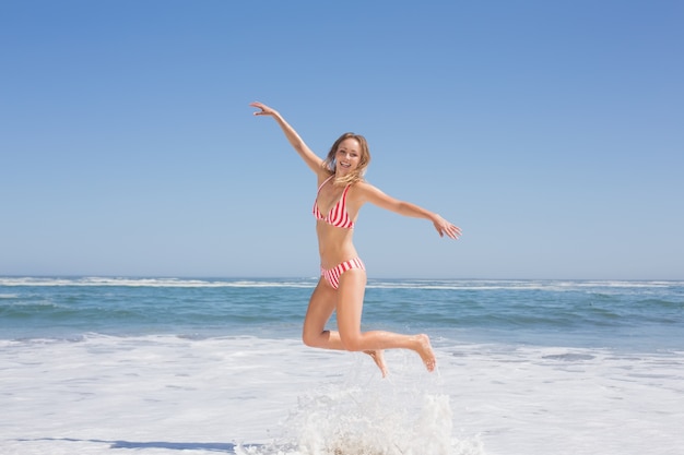 Felice donna in forma in bikini che salta sulla spiaggia