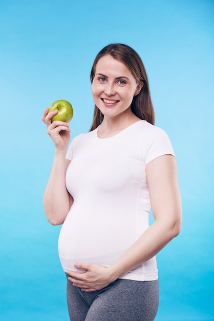 Felice donna incinta con la mela Granny Smith che tocca la parte inferiore della sua pancia mentre si trovava in isolamento