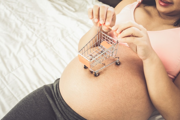 Felice donna incinta con un piccolo giocattolo shopping car sulla sua pancia