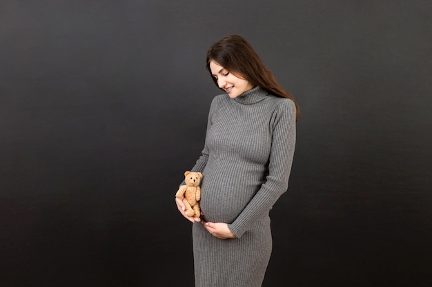 Felice donna incinta in possesso di un orsacchiotto contro il suo ventre a Sfondo colorato Giovane madre si aspetta un bambino Copia spazio