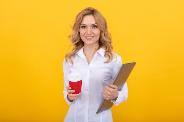 Felice donna insegnante con laptop tenere tazza di carta da asporto sfondo giallo pausa caffè