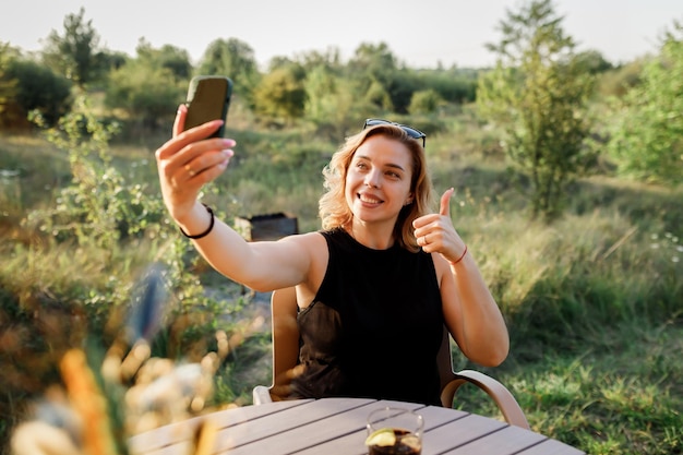 Felice donna libera professionista che parla con gli amici tramite videochiamata mentre si rilassa su un'accogliente tenda glamping in una giornata di sole Tenda da campeggio di lusso per vacanze estive all'aperto e vacanze Concetto di stile di vita