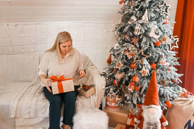 Felice donna madre si sta preparando per Natale, Capodanno confeziona regali a casa mentre è seduta vicino all'albero di Natale. Vacanze invernali, concetto di decorazione domestica