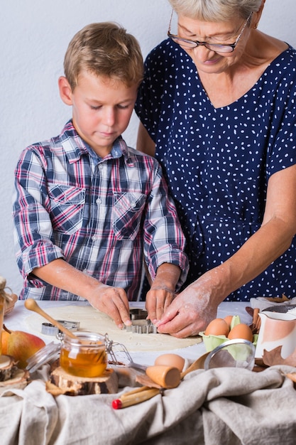 Felice donna matura anziana, nonna e ragazzo, nipote che cucina, impasta la pasta, cuoce la torta, la torta, i biscotti. Tempo in famiglia nell'accogliente cucina. Attività autunnale a casa.