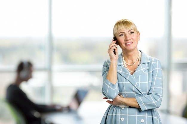 Felice donna matura parlando al cellulare. Allegra donna matura parlando al telefono sulla finestra dell'ufficio. Felice metà donna utilizzando il telefono cellulare.