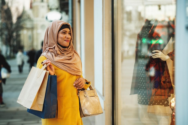 Felice donna musulmana nera che indossa l'hijab e cammina per strada con la borsa della spesa.