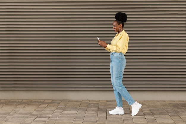 Felice donna nera utilizzando il telefono in piedi in un'area urbana all'aperto