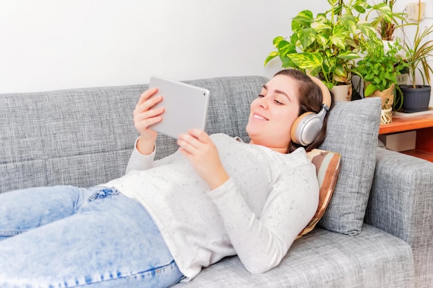 Felice donna pensierosa che utilizza la tavoletta digitale a casa