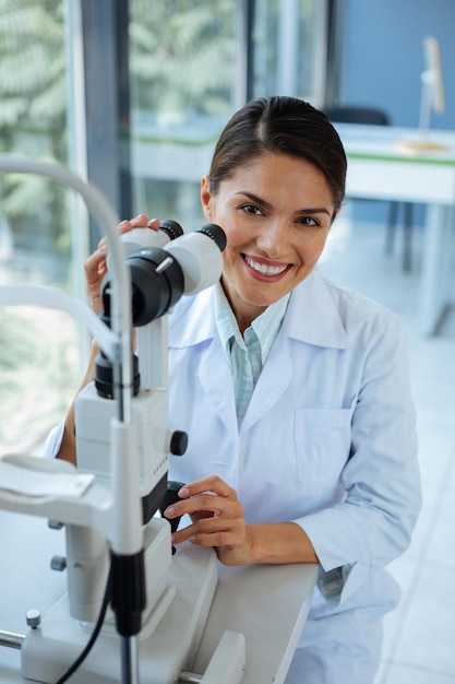 Felice donna positiva seduta vicino al microscopio mentre è al lavoro in clinica