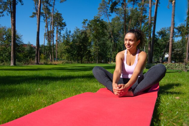 Felice donna seduta su un tappetino fitness, godendo di allenamento in una soleggiata giornata estiva