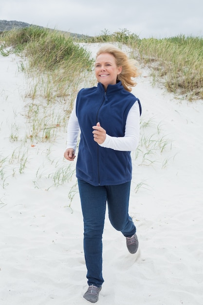 Felice donna senior a fare jogging in spiaggia