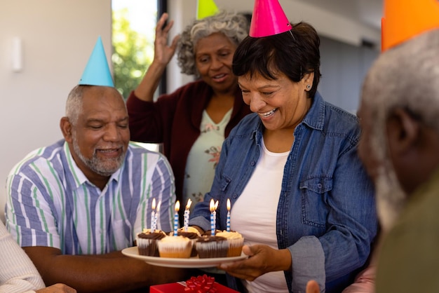 Felice donna senior multirazziale che tiene cupcakes con candele mentre si gode il compleanno con gli amici