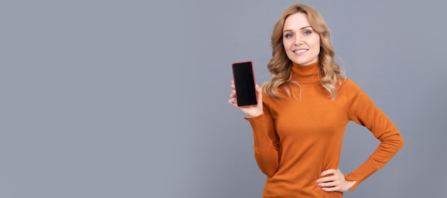 Felice donna tenere moderno smartphone sfondo grigio dispositivo mobile Ritratto di donna isolato banner di intestazione con spazio di copia