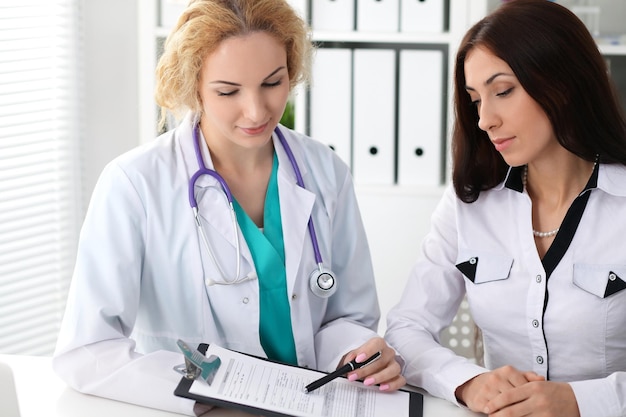 Felice dottoressa bionda e paziente che discutono dei risultati dell'esame medico. Medicina, assistenza sanitaria e concetto di aiuto.