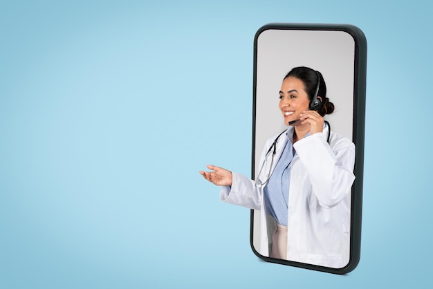 Felice dottoressa latina con auricolare sul grande schermo del cellulare con appuntamento online blu