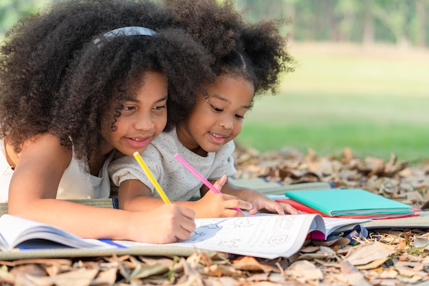 Felice due bambine afroamericane sdraiato disegno nel libro da colorare per i bambini nel parco
