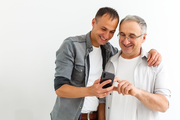 Felice due generazioni di uomini di famiglia vecchio padre che abbraccia il giovane figlio adulto che si diverte a divertirsi usando il legame dello smartphone guardando divertenti video sui social media utilizzando le app mobili