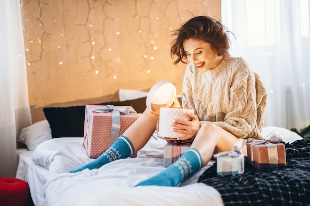 Felice e bella mora sul letto con scatole regalo intorno a lei