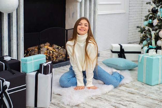 felice e carina giovane donna che celebra il natale a casa davanti al caminetto con regali