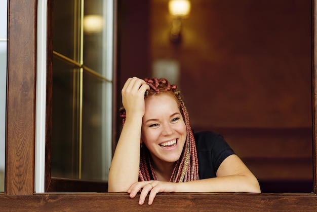 Felice e ridente ragazza dai capelli rossi che guarda fuori dalla finestra