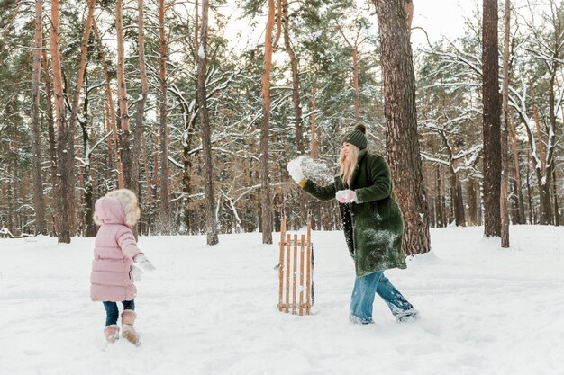 Felice e sorridente giovane madre e la sua piccola figlia che si divertono fuori nel parco invernale