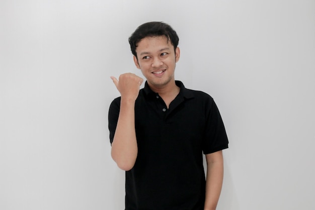 Felice e sorriso di giovane uomo asiatico con il punto della mano su uno spazio vuoto Indonesia L'uomo indossa una camicia nera Sfondo grigio isolato