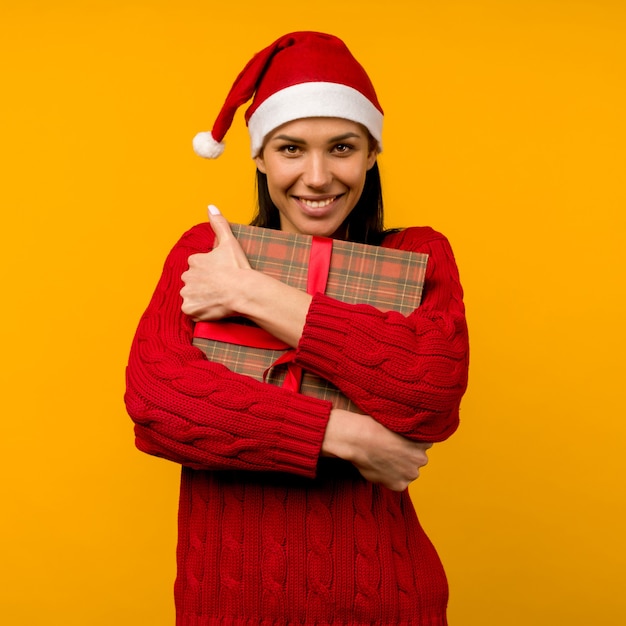 Felice eccitato giovane donna in cappello di Babbo Natale con confezione regalo su sfondo giallo - immagine