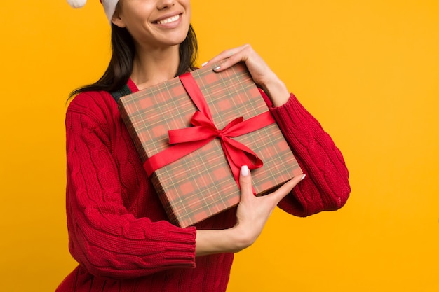 Felice eccitato giovane donna in cappello di Babbo Natale con confezione regalo su sfondo giallo - immagine