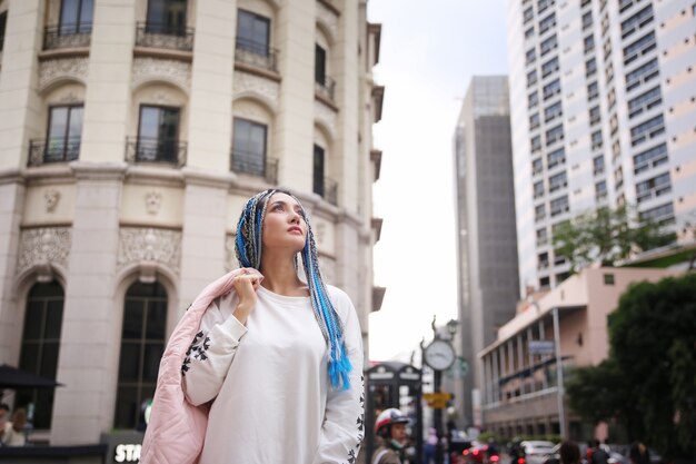 Felice elegante giovane donna hipster con lunghi capelli blu e giacca rosa sulla città