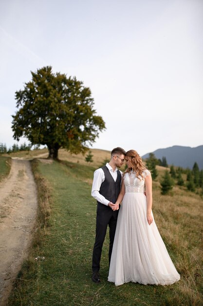 Felice elegante sposa e sposo che corrono e si divertono in montagna in una giornata di sole estivo