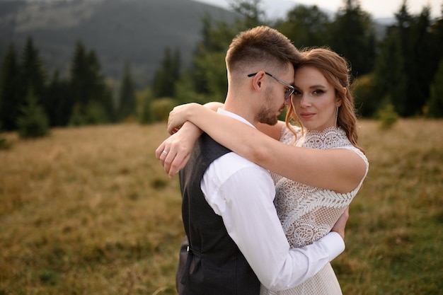 Felice elegante sposa e sposo che corrono e si divertono in montagna in una giornata di sole estivo