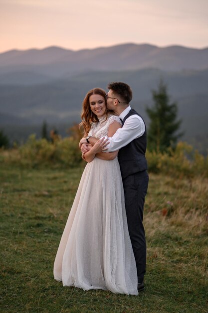 Felice elegante sposa e sposo che corrono e si divertono in montagna in una giornata di sole estivo