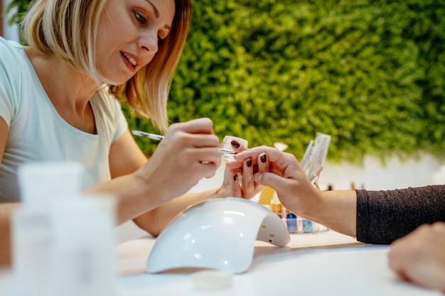 Felice estetista dipingere le unghie delle clienti al salone di bellezza.