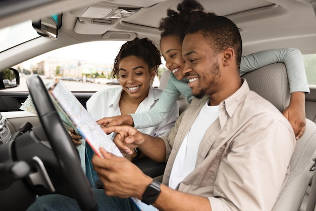 Felice famiglia africana che tiene mappa seduto in macchina scegliendo destinazione