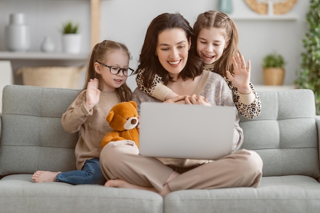 Felice famiglia amorevole. Giovani ragazze della madre e delle figlie che per mezzo del computer portatile. La mamma divertente e i bambini adorabili si divertono a stare a casa.